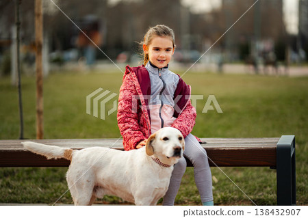 Girl petting dog sitting on park bench Girl petting dog sitting on park bench 138432907