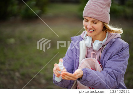 Smiling woman spraying hand sanitizer on her palm outdoors 138432921