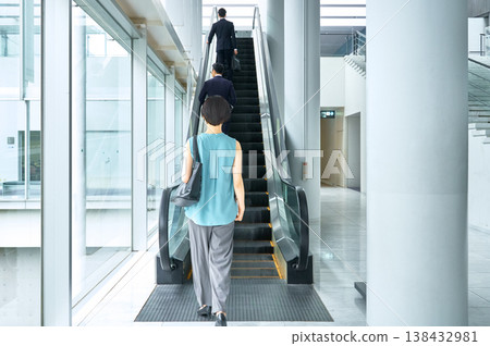 一位商務人士搭乘自動扶梯穿過辦公大樓的背影。 138432981