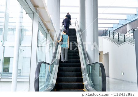 辦公大樓裡，商務人士和職業婦女的背影正沿著自動扶梯向上移動。 138432982