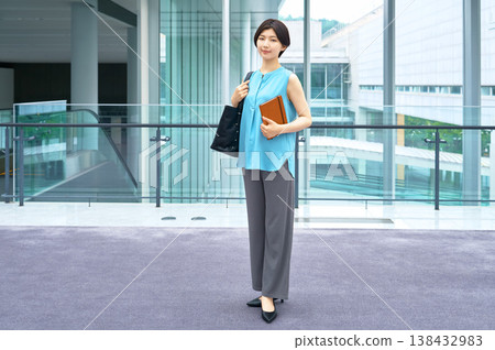 一張全身照,一位自信的日本女商人站在現代化的辦公大樓裡,手裡拿著筆記本。 一張全身照,一位自信的日本女商人站在現代化的辦公大樓裡,手裡拿著筆記本。 138432983