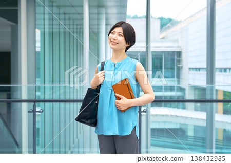 A refreshing businesswoman smiles, holding a notebook, with an office building in the background. A refreshing businesswoman smiles, holding a notebook, with an office building in the background. 138432985