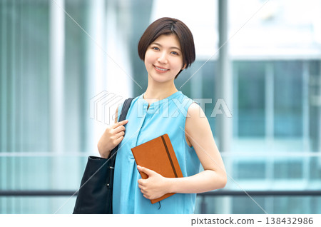 一位笑容燦爛的女商人手持筆記本,站在辦公大樓裡。 一位笑容燦爛的女商人手持筆記本,站在辦公大樓裡。 138432986
