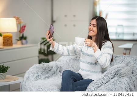 Young adult woman taking selfie with smartphone drinking coffee Young adult woman taking selfie with smartphone drinking coffee 138433451