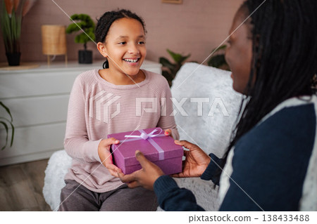 Happy little girl receiving a birthday gift from parent Happy little girl receiving a birthday gift from parent 138433488