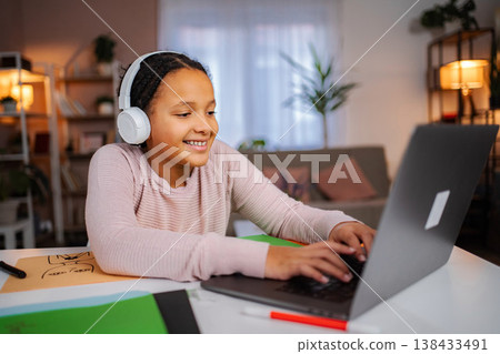 Girl wearing headphones learning online using laptop at home Girl wearing headphones learning online using laptop at home 138433491