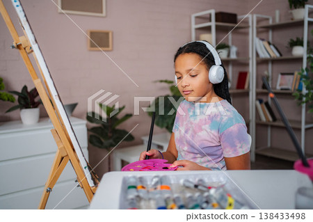 Young girl wearing headphones painting on canvas at home Young girl wearing headphones painting on canvas at home 138433498