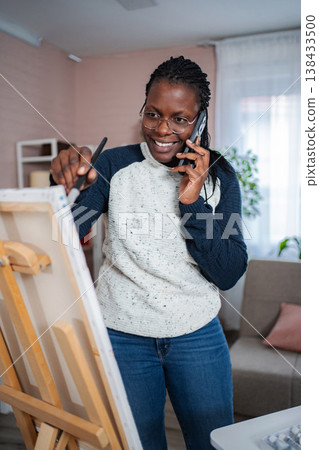 Woman painting on easel while talking on phone 138433500