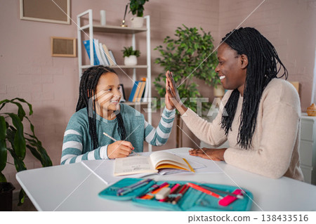 Mother and daughter high fiving while studying lessons at home 138433516