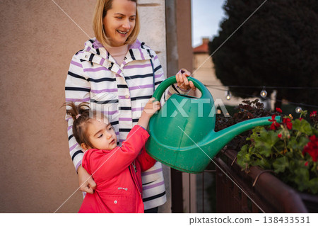 Mother and daughter bonding watering potted plants on balcony 138433531