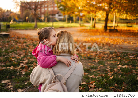 Daughter sharing secret with mother in autumn park Daughter sharing secret with mother in autumn park 138433700