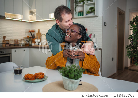Interracial couple sharing morning coffee and embracing in kitchen Interracial couple sharing morning coffee and embracing in kitchen 138433763