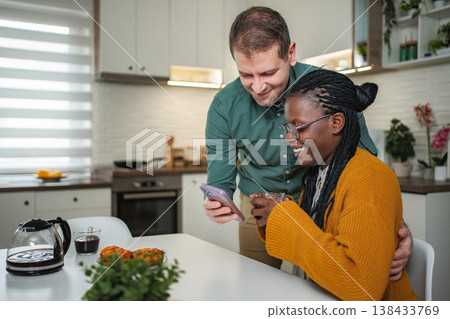 Diverse couple smiling, using smartphone, having breakfast in kitchen Diverse couple smiling, using smartphone, having breakfast in kitchen 138433769