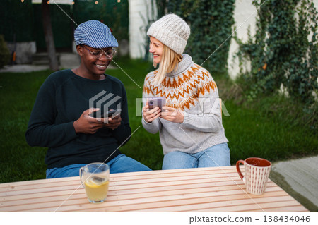 Diverse women friends sitting outdoors laughing using mobile phones Diverse women friends sitting outdoors laughing using mobile phones 138434046