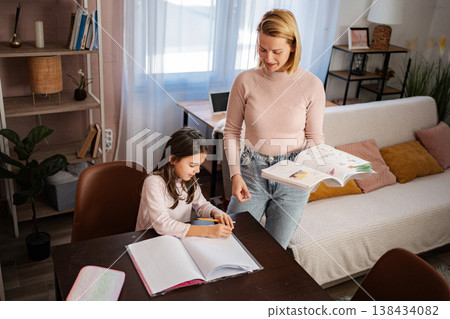 Mother assisting daughter with homework, studying and learning at home 138434082