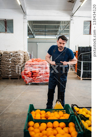 Male worker moving crates of fresh oranges in warehouse 138434120
