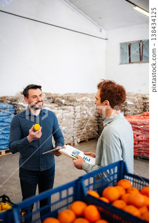Produce managers discussing quality control of citrus fruits in warehouse 138434125