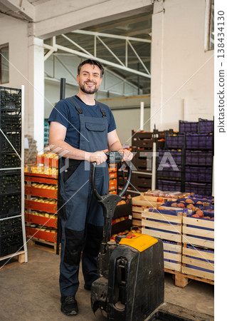 Happy male worker moving fresh fruit crates in warehouse 138434130