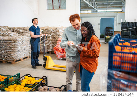 Business partners collaborating in a warehouse checking produce inventory Business partners collaborating in a warehouse checking produce inventory 138434144