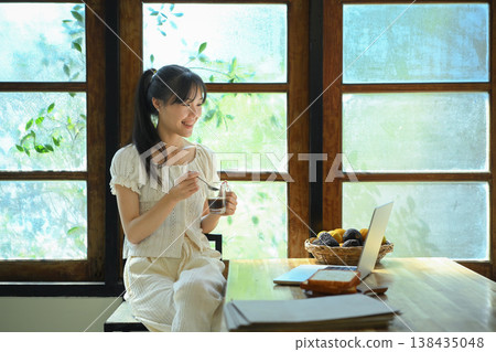 Young woman drinks coffee while using laptop at kitchen counter. 138435048