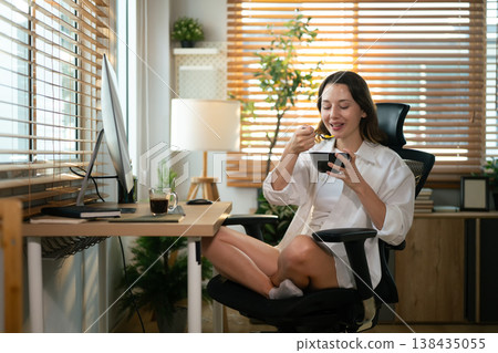Remote worker eating breakfast while sitting at computer workspace. Remote worker eating breakfast while sitting at computer workspace. 138435055