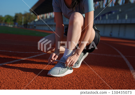 Close up of woman tying running shoe laces on outdoor track before exercise, fitness preparation Close up of woman tying running shoe laces on outdoor track before exercise, fitness preparation 138435073
