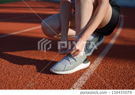 Close up of woman tying running shoe laces on outdoor track before exercise, fitness preparation 138435079