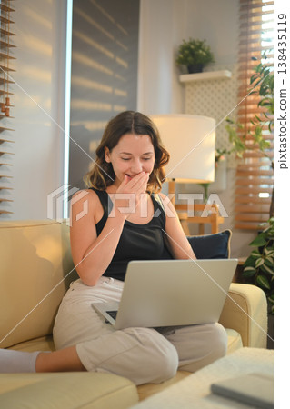 Woman reacting with surprise while using laptop on sofa at home Woman reacting with surprise while using laptop on sofa at home 138435119