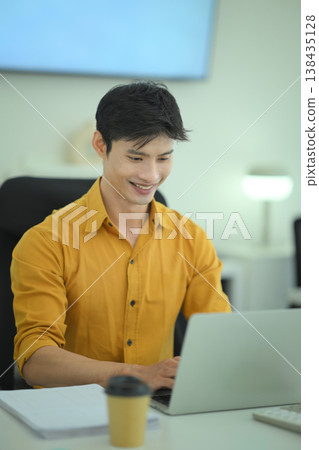 Smiling businessman working on laptop in office Smiling businessman working on laptop in office 138435128