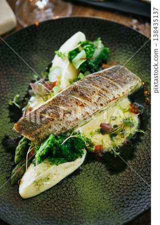 An artfully plated fish dish garnished with fresh greens and sauce, offering a delicious experience An artfully plated fish dish garnished with fresh greens and sauce, offering a delicious experience 138435137