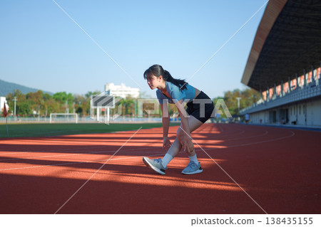 Young Asian woman stretching leg muscles on outdoor running track before workout Young Asian woman stretching leg muscles on outdoor running track before workout 138435155