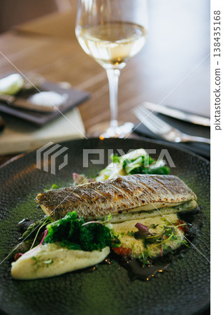 An artfully plated fish dish garnished with fresh greens and sauce, offering a delicious experience An artfully plated fish dish garnished with fresh greens and sauce, offering a delicious experience 138435168