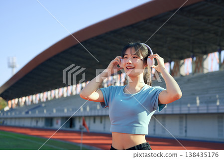 Young Asian woman wearing headphones at outdoor running track, enjoying music before workout 138435176