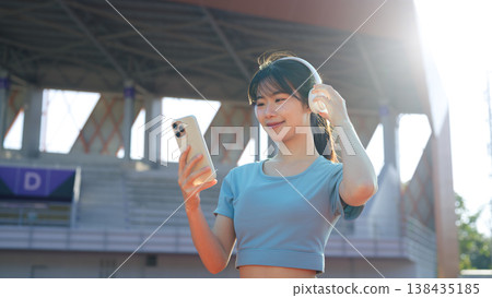 Asian woman play a music with smartphone at outdoor running track, enjoying music before workout Asian woman play a music with smartphone at outdoor running track, enjoying music before workout 138435185