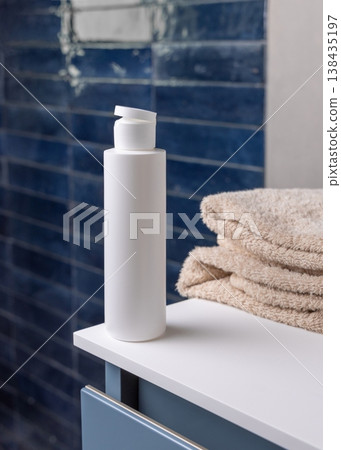 White flip top cosmetic bottle near beige bath towel in blue bathroom, cosmetic mockup 138435197