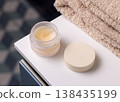 Opened handmade lip balm jar in blue bathroom with towel. Blank lid cosmetic mockup 138435199