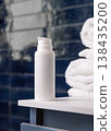 White pump cosmetic bottle near white bath towel in dark blue bathroom, cosmetic mockup 138435200