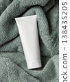 White blank cream tube on sage green bath towel top view, unbranded cosmetic mockup 138435205