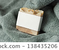 Solid soap bar mockup with blank paper label on sage green bath towel, unbranded packaging 138435206