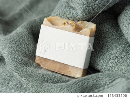 Solid soap bar mockup with blank paper label on sage green bath towel, unbranded packaging Solid soap bar mockup with blank paper label on sage green bath towel, unbranded packaging 138435206
