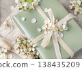 Light green gift box with white spring flowers and ribbon bow in soft pastel tones closeup 138435209