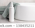 White pump cosmetic bottle mockup near sage green bath towel in bathroom. Unbranded packaging 138435211
