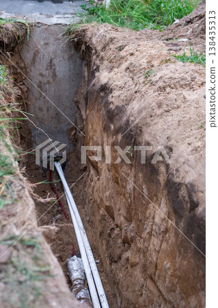 Trench for laying insulated supply pipes, plumbing line installation, groundwork, protection against frost, maintenance, construction earthworks, repair job. 138435313