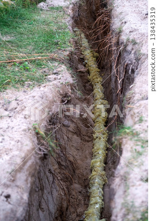 Freshly dug trench for insulated pipeline, supply line laying, outdoor groundwork preparation, repair, earthworks, protection, engineering, household maintenance. 138435319