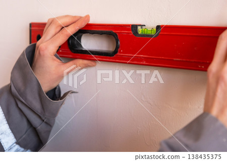 Checking wall alignment using level, surface preparation before installation, marking for renovation, professional interior construction tools. Checking wall alignment using level, surface preparation before installation, marking for renovation, professional interior construction tools. 138435375