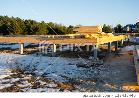 Foundation piles and base frame for wooden house, site preparation, starting phase, carpentry works, construction project, timber support structure, beams. 138435446