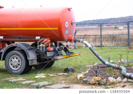 Sewage vacuum truck pumping waste from private house septic tank, liquid waste removal and disposal service, sanitation business concept. Sewage vacuum truck pumping waste from private house septic tank, liquid waste removal and disposal service, sanitation business concept. 138435504