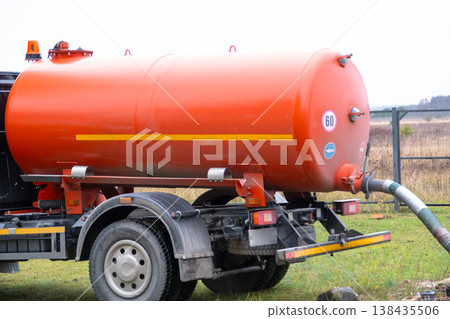 Bright orange vacuum tanker removes sewage from home septic system, septic tank servicing, waste export, sanitation and disposal company. Bright orange vacuum tanker removes sewage from home septic system, septic tank servicing, waste export, sanitation and disposal company. 138435506