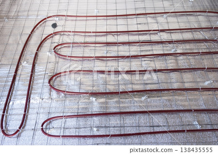 Underfloor heating system mounting, laying pipes in loops on insulation grid, radiant floor heat, home renovation, efficient modern construction technique. 138435555
