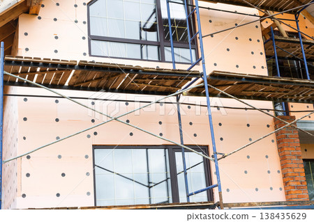 Building facade with foam insulation, scaffolding for external wall mounting, energy-efficient cladding, construction renovation, panel installation, waterproofing. Building facade with foam insulation, scaffolding for external wall mounting, energy-efficient cladding, construction renovation, panel installation, waterproofing. 138435629